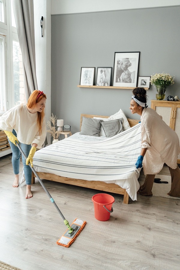Two housemates sharing the cleaning, one mopping while the other makes the bed